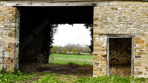 Landscape close up of 18th century stone barn, with open cart doors and views across Oxfordshire countryside. Small doorway, repointing and cracking to walls. Ivy silhouette around far door. Broughton photo
