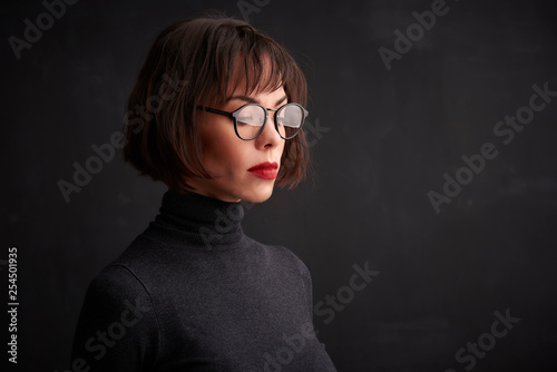 Close-up studio shot of young woman wearing eyewear and red lipstick while standing at dark background