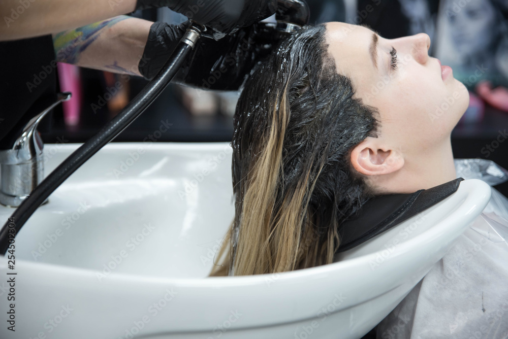 Fototapeta premium Beauty concept - Professional hairdresser applying shampoo, washes color paint off and massaging hair of a customer. Woman having her hair washed in a hairdressing beauty salon