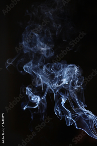 White and blue smoke on a black background. Sharp curls and smoke and out of focus.
