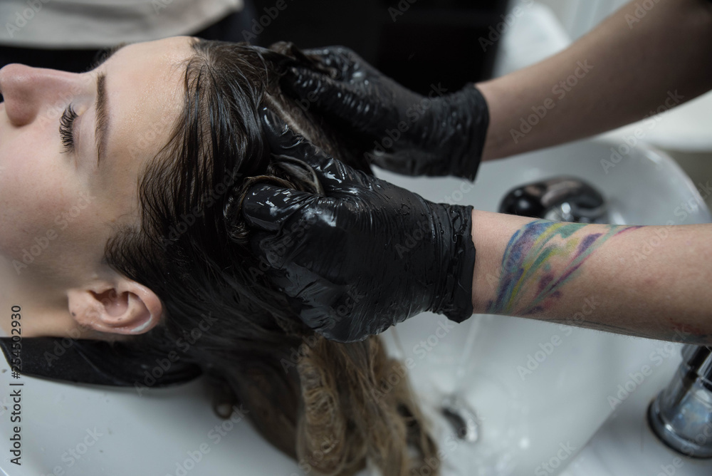 Naklejka premium Beauty concept - Professional hairdresser applying shampoo, washes color paint off and massaging hair of a customer. Woman having her hair washed in a hairdressing beauty salon