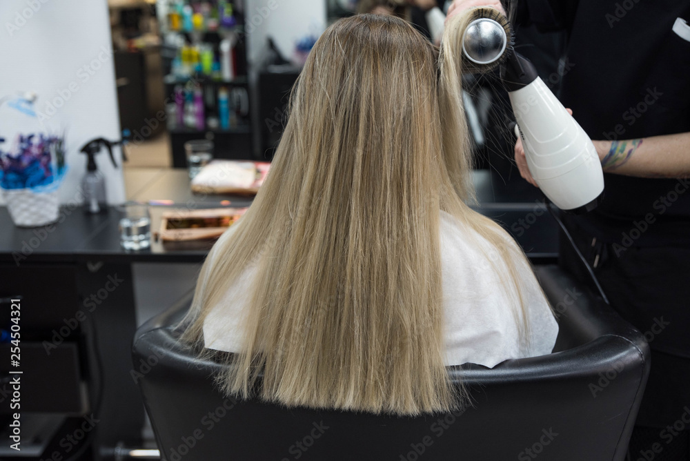 Professional hairdresser brushing beautiful client’s hair with round brush Professional hairdresser brushing beautiful client’s hair with round brush