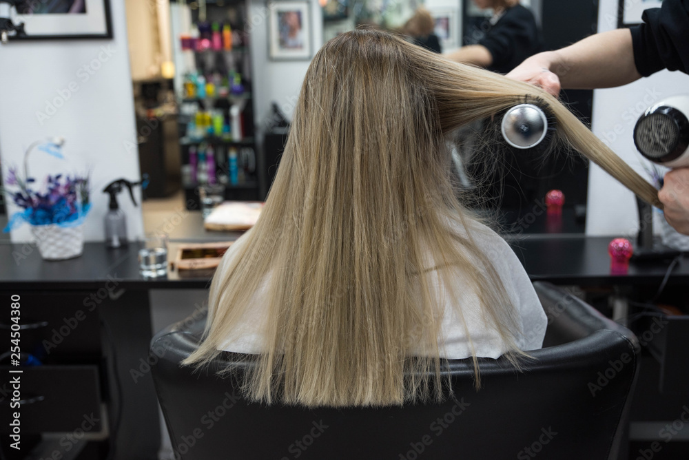 Professional hairdresser brushing beautiful client’s hair with round brush Professional hairdresser brushing beautiful client’s hair with round brush