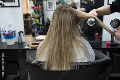 Professional hairdresser brushing beautiful client’s hair with round brush