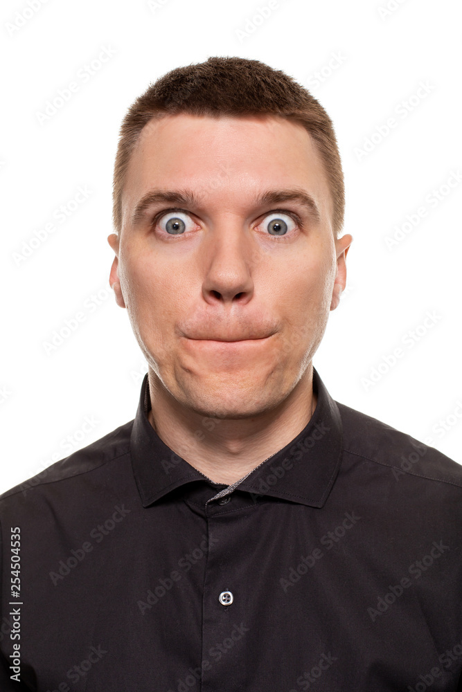 Handsome young man in a black shirt is making faces, while standing isolated on a white background Handsome young man in a black shirt is making faces, while standing isolated on a white background