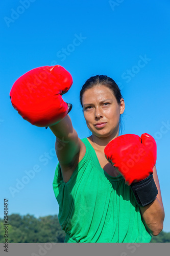 Young woman punches with red boxing gloves outside
