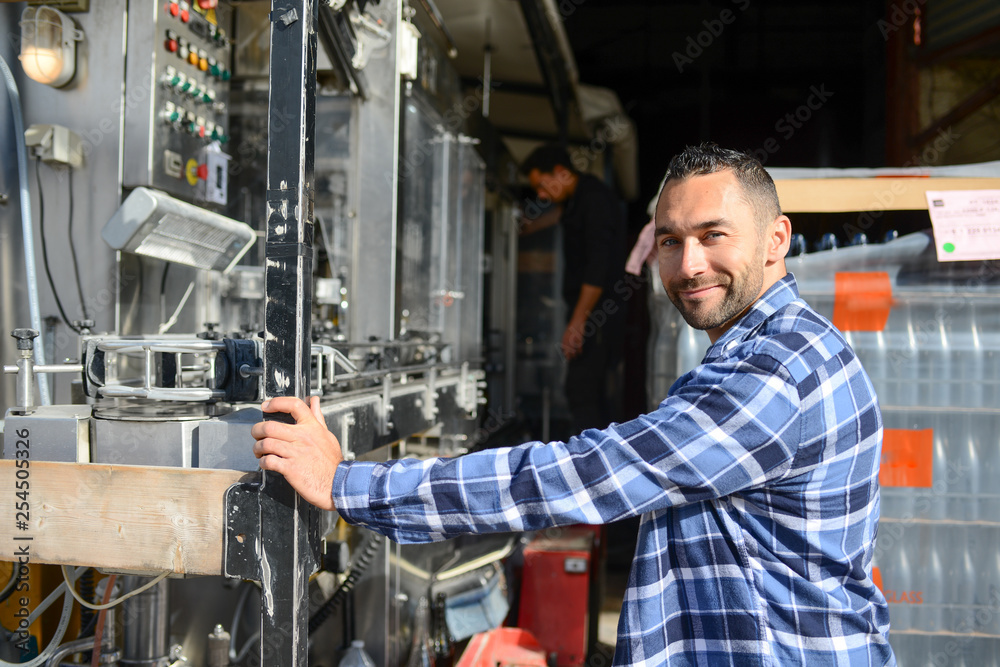 young man wine maker working filling wine bottle with automatic bottling machine young man wine maker working filling wine bottle with automatic bottling machine