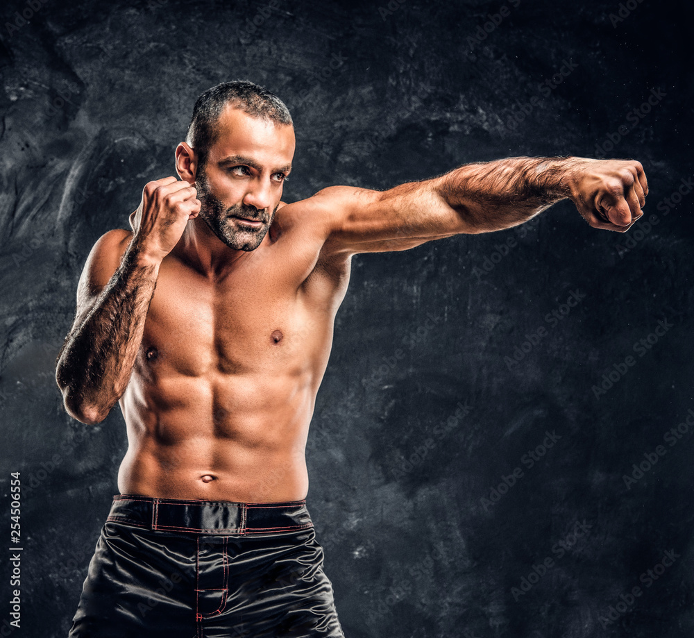 Professional fighter showing kick fighting technique. Studio photo against a dark textured wall