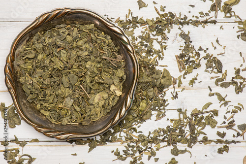 Lot of pieces of dry green tea in old iron bowl flatlay on white wood photo