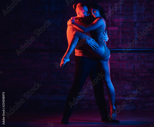 Young attractive couple dancing on the dance floor in a night club. Dancers performing in the dark with illumination