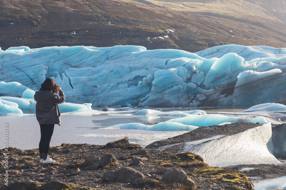 Back view of female tourists photographer taking picture of beautiful evening scenery of Skaftafell glacier Vatnajokull national park in Iceland is blue and cold is iceberg and best place for turism.