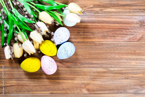 Spring composition of tulips and Easter colored eggs on a brown wooden background with copy space. Postcard layout. Flat lay