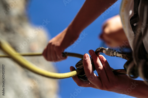 Detail of a woman belaying a climber with an autolocking belay device.