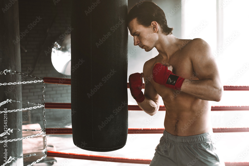 Male boxer boxing in punching bag. The boxer touches his head to the punching bag