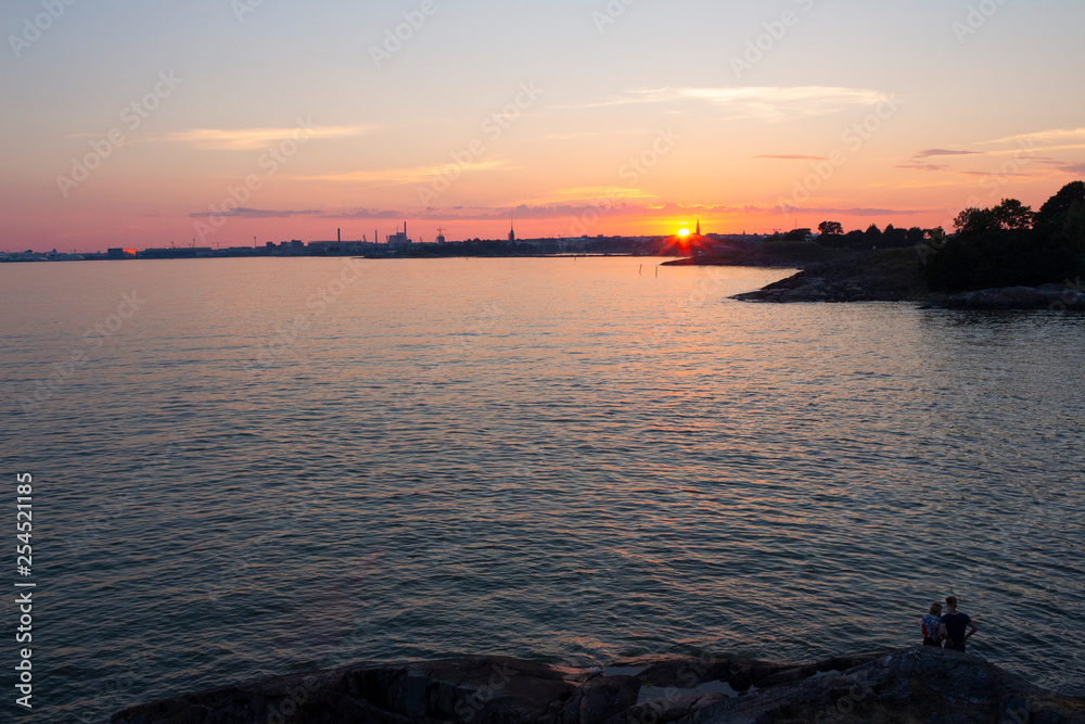 Naklejka premium View of the Gulf of Finland at sunset of a summer day from the steep rocky shore of the island Suomenlinna Sveaborg in Finland. View from the island towards Helsinki on the horizon.