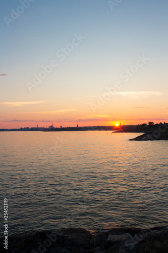 Fototapeta Naklejka Na Ścianę i Meble -  View of the Gulf of Finland at sunset of a summer day from the steep rocky shore of the island Suomenlinna Sveaborg in Finland. View from the island towards Helsinki on the horizon.