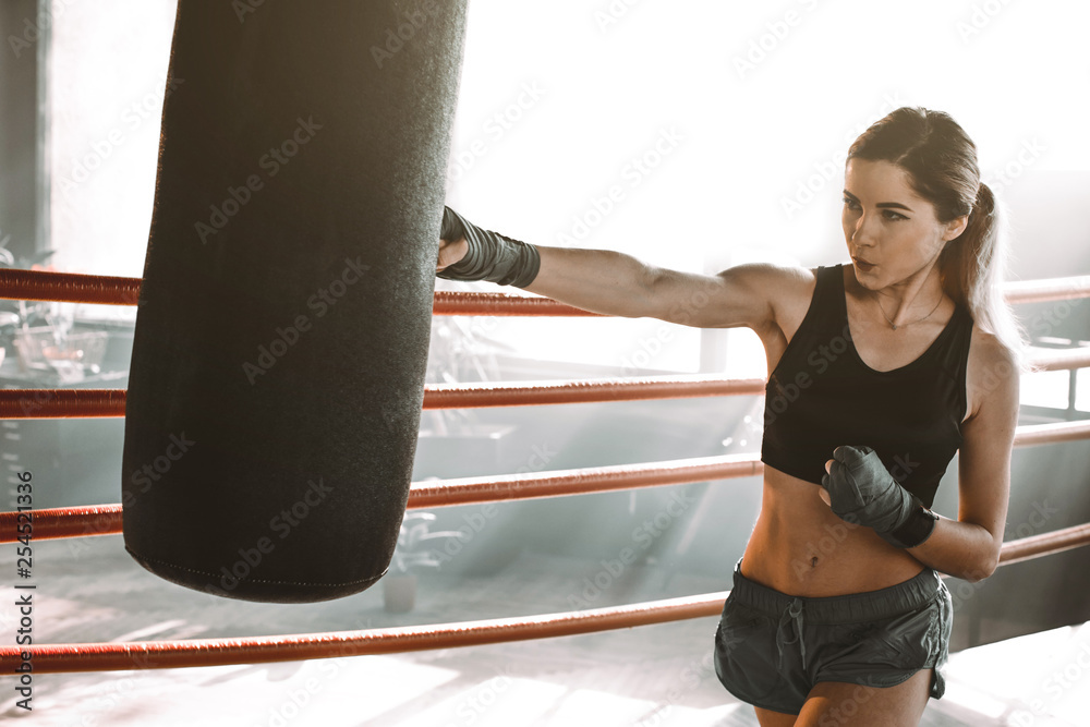 Beautiful, confident woman boxer athletic punching bag during training preparation for battle.