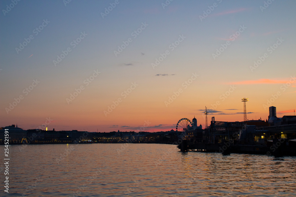 View of the embankment of Helsinki, houses and the silhouette of the Cathedral of St. Nicholas from the Gulf of Finland at dusk on a bright summer night in the capital of Finland.