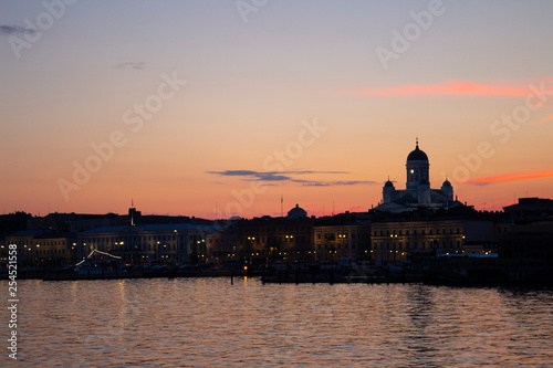 View of the embankment of Helsinki, houses and the silhouette of the Cathedral of St. Nicholas from the Gulf of Finland at dusk on a bright summer night in the capital of Finland. © NATALIA