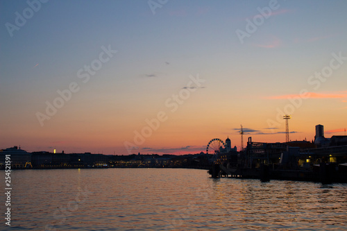 View of the embankment of Helsinki, houses and the silhouette of the Cathedral of St. Nicholas from the Gulf of Finland at dusk on a bright summer night in the capital of Finland.