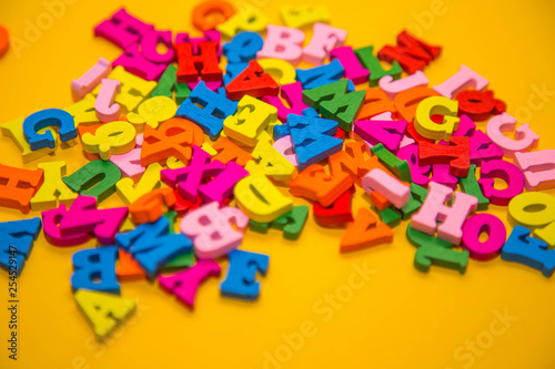 Many multicolored wooden letters on a yellow background. toy letters. english alphabet. View from above. Flat lay. Copy space for text.