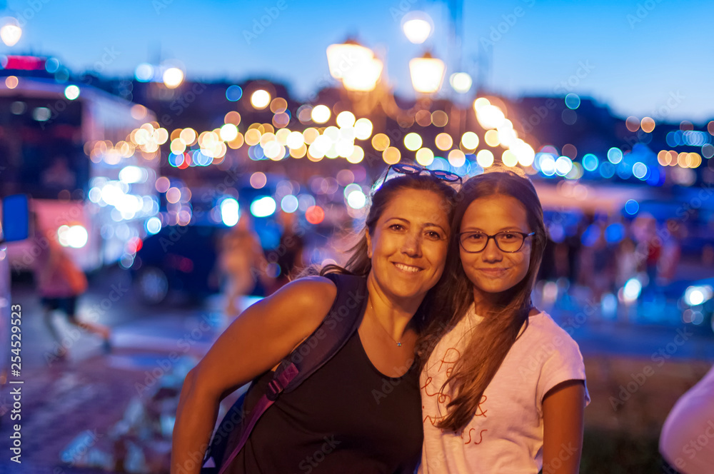 Fototapeta premium Mother and daughter look at camera together, blurred background at night,