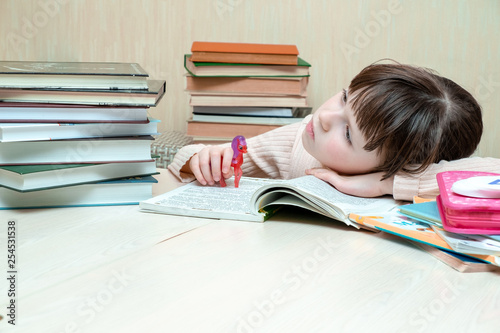 SThe schoolgirl laid her head on the book and thoughtfully looks into the distance. A child holds a toy horse in his right hand photo
