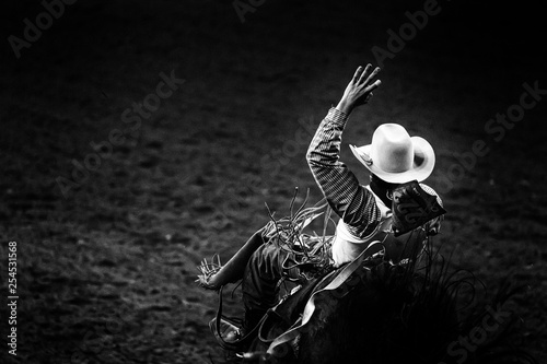 Monochrome rodeo cowboy in a white hat riding a bronco in ththe spotlight  photo