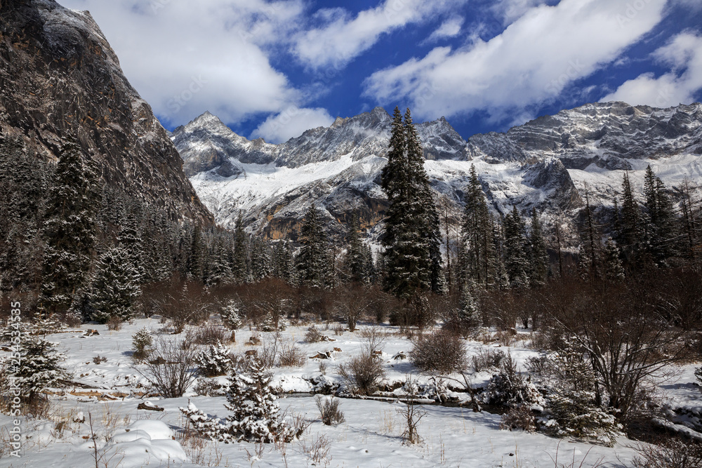 Fototapeta premium Siguniangshan - Four Girls Mountain National Park in Sichuan Province, China. ShuangQiao Valley Scenic Area, Snow Capped Jagged Mountains with clouds forming at the summit. Blue Sky, Snow Mountains