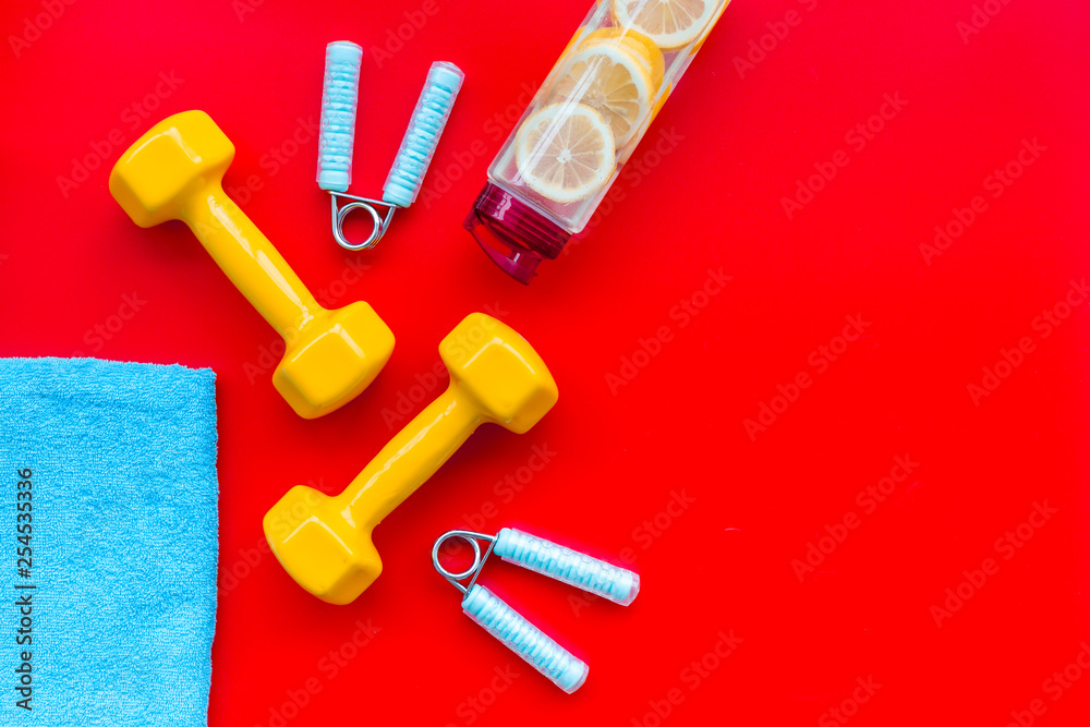 Fitness set with bars, towel, bottle of water and wrist builder on red background top view mock up Fitness set with bars, towel, bottle of water and wrist builder on red background top view mock up
