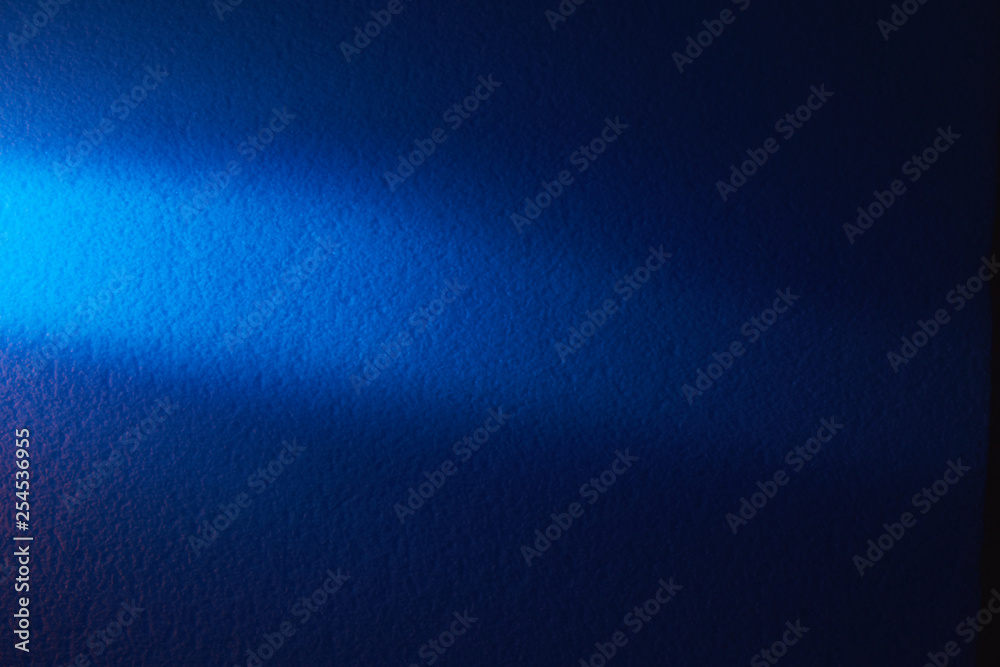 A beam of light blue light horizontally shines on a blurry textural blue background