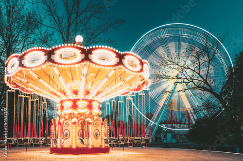 Billede på lærred Illuminated Attraction Ferris Wheel And Carousel Merry-go-round On Summer Evening In City Amusement Park