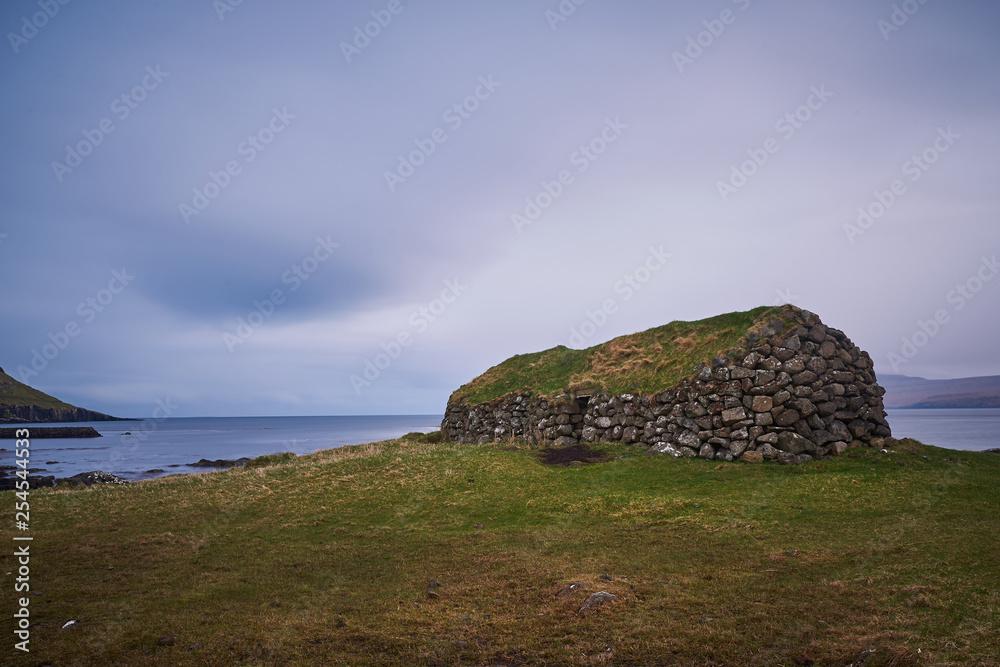 Rural herdsman house in sheep pasture or grazing land made from stones with grass roof from medieval viking age in village Kirkjubour in Streymoy island in Faroe islands, north atlantic ocean in rain.