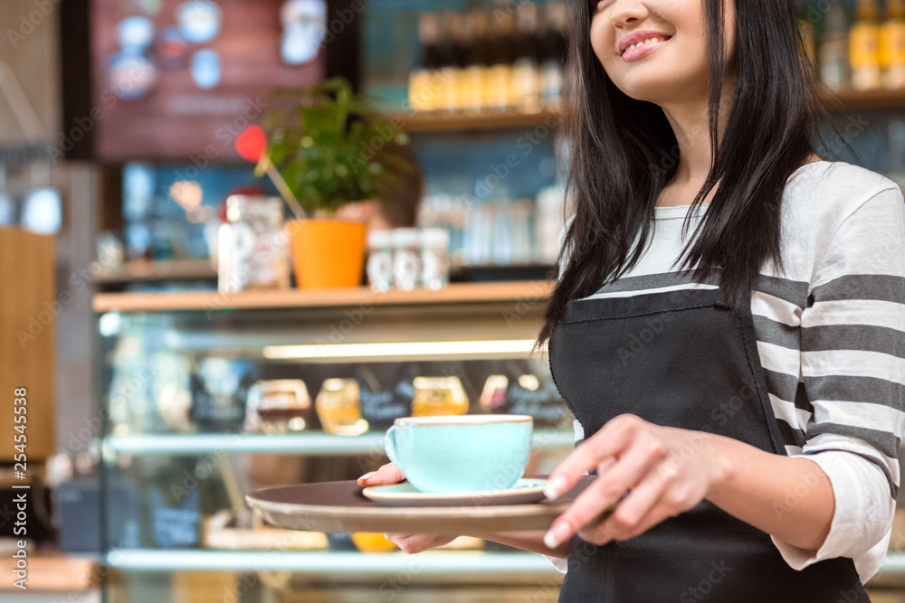 Bringing warmth to you. Cropped closeup of a smiling happy waitress holding a tray with a cup of coffee Bringing warmth to you. Cropped closeup of a smiling happy waitress holding a tray with a cup of coffee