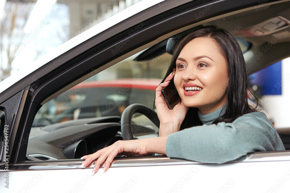 Greatest news. Low angle closeup shot of a beautiful happy brunette woman talking on the phone sitting in a brand new car at the car salon
