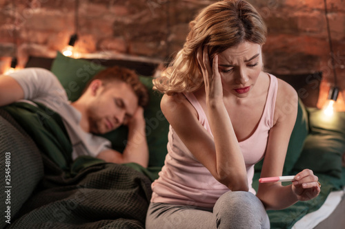 Young wife feeling worried after pregnancy test while husband sleeping