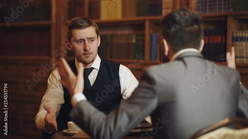 Professors speaking or discuss education in vintage interior. Intelligent elite and education concept. Men with antique bookshelves on background. Intelligent men, scientists spend leisure in library. photo