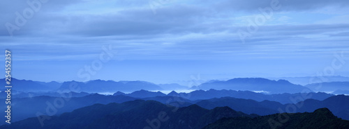 Abstract Image  Mountain Silhouettes at dawn - rolling jagged mountain peaks  cold blue color hues. Panoramic Abstract Background Image  overcast skies  layers of rolling mountains in the distance.