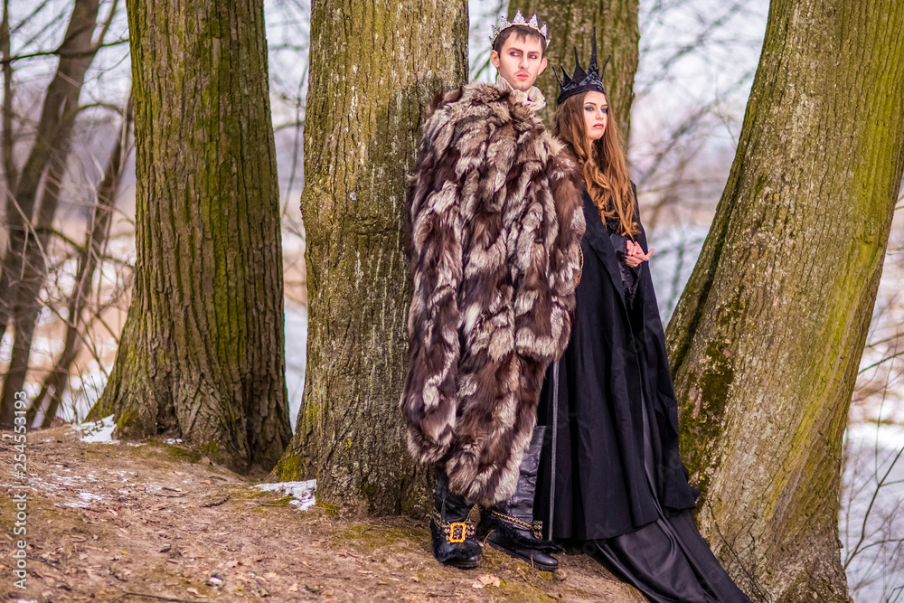 Art Photography and Cosplay.Caucasian Couple as King and Queen in Fur Medieval Outfit With Crowns Posing Together Outdoor.