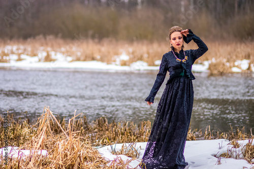 Dreaming Vulnerable Caucasian Brunette Female in Art Dress with Necklace and Crown Posing Against River Outdoors. photo