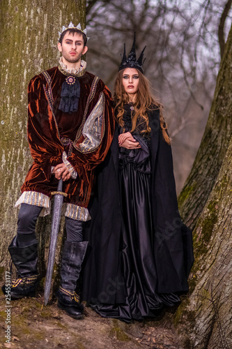 Cosplay Ideas.Caucasian Couple as King and Queen in Fur Medieval Outfit With Crowns Posing Together Outdoor.