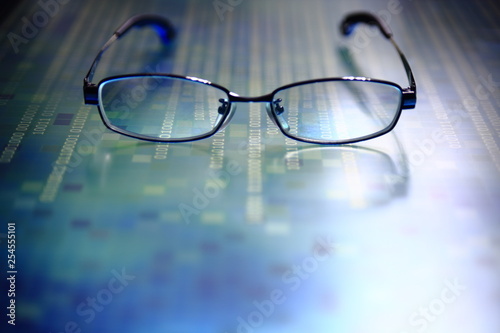 big data analysis. glasses placed on a LED digital panel display white light one and zero binary text number in moving motion pattern. modern technology blue block grid pattern backgrounds