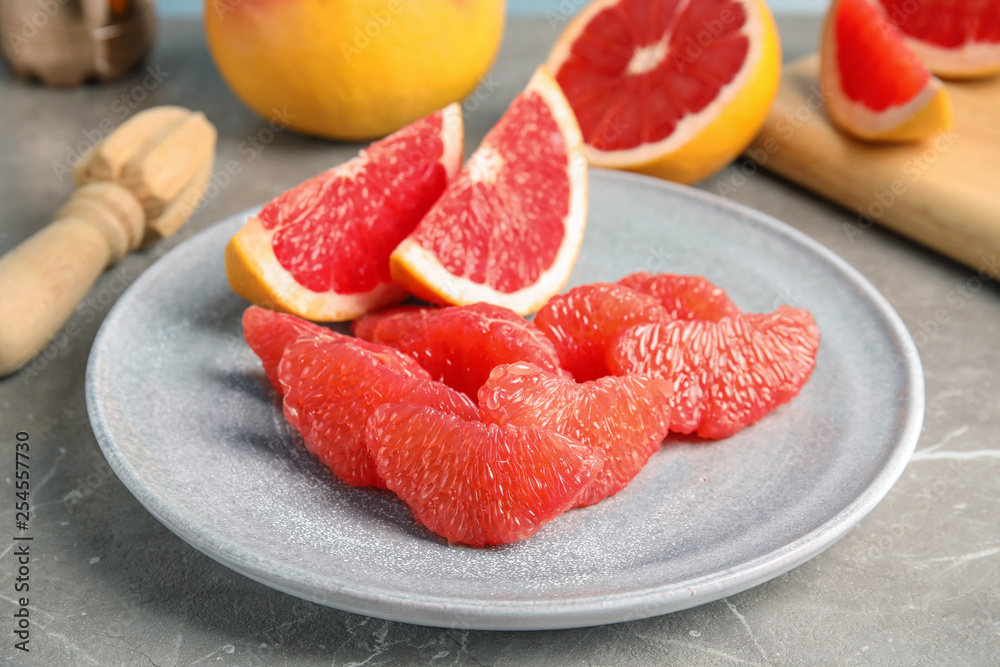 Plate with ripe grapefruit on grey table