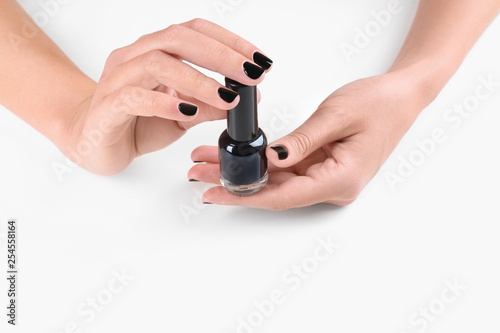 Woman with black manicure holding nail polish bottle on white background, closeup