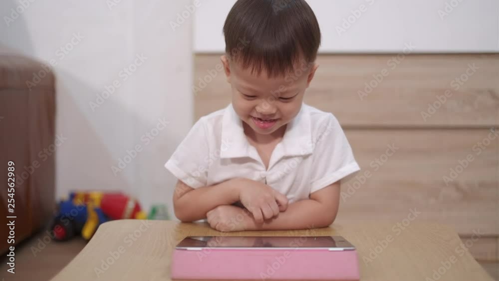 Cute little smiling Asian 2 - 3 years old toddler baby boy child sitting on floor watching a video from tablet pc. Kids playing with tablet computer, Gadget-addicted children concept Cute little smiling Asian 2 - 3 years old toddler baby boy child sitting on floor watching a video from tablet pc. Kids playing with tablet computer, Gadget-addicted children concept