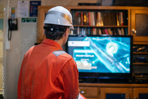 Marine chief officer wearing coverall and helmet on a ship or vessel having fun watching TV. Recreation during at sea photo