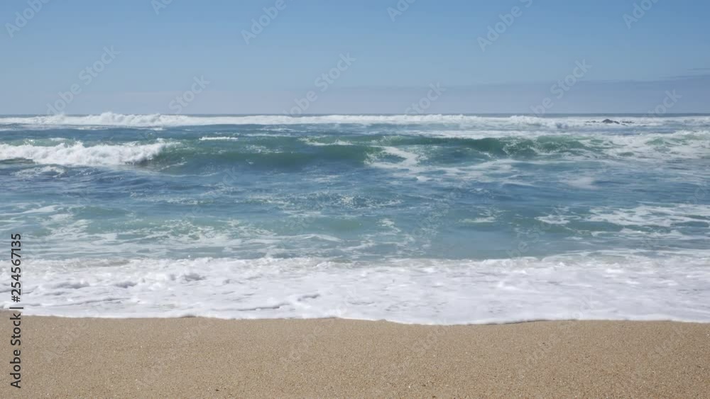 Straight on waves breaking on sandy beach in Portugal on a sunny day with blue sky. Camera parallel to shoreline. Straight on waves breaking on sandy beach in Portugal on a sunny day with blue sky. Camera parallel to shoreline.
