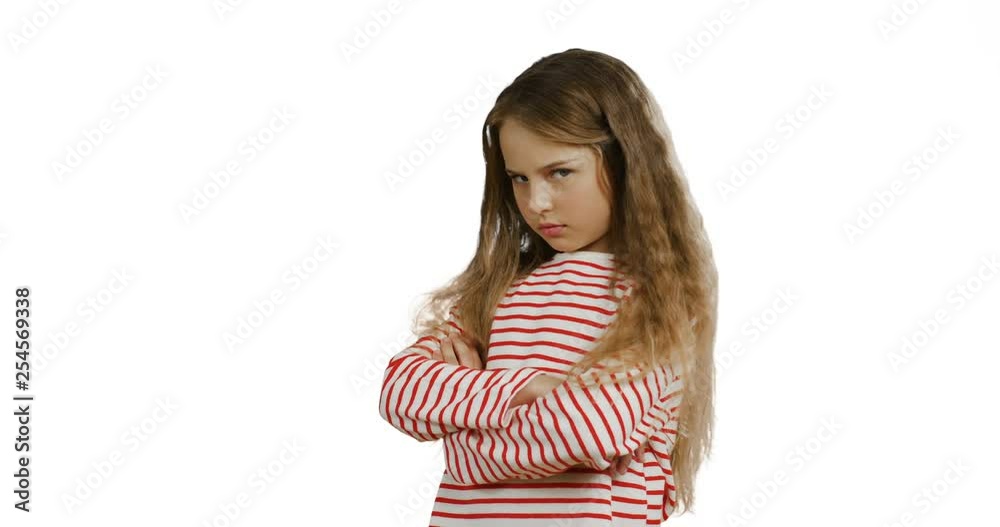 Caucasian little teenage girl with long fair hair standing on the white background with crossed hands and being offended. Caucasian little teenage girl with long fair hair standing on the white background with crossed hands and being offended.