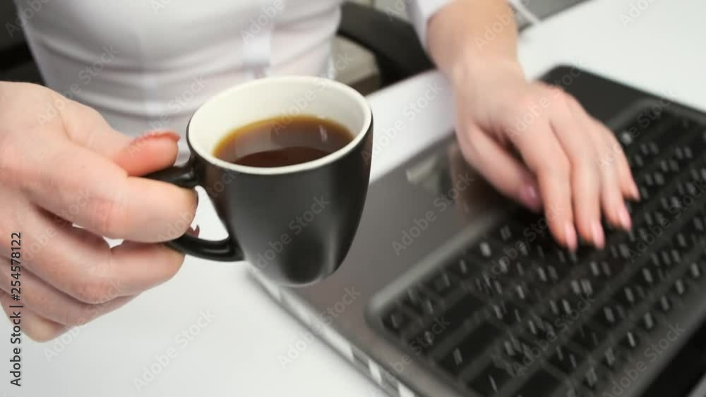 woman drinks hot coffee and works on computer in office. woman drinks hot coffee and works on computer in office.