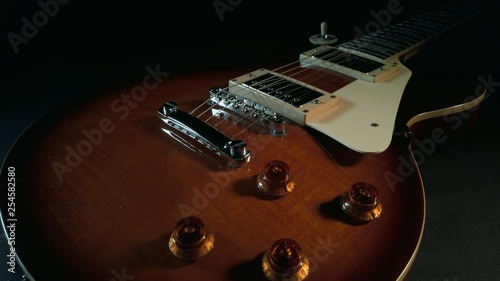 Slow tracking shot across the body of a Gibson Les Paul electric guitar, covering the volume and tone controls, bridge, guard, pickups and strings photo